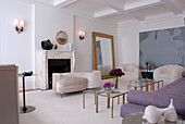 Elegant, feminine living room in white and mauve with gilt-framed mirror and small glass tables with brass frames