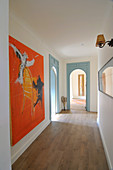 Long hallway with wooden floor, arched doorways and artworks on walls