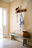Open cloakroom with hat and towel hanging from a wall coat rack above a rustic wooden bench in a simple foyer