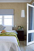 Damenstrohhut auf Bett vor Fenster und offene Terrassentür in schlichtem Schlafzimmer