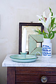 Vintage candlestick holder next to a vase with white lilies on a chest of drawers