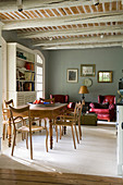 Antique dining table and wooden chairs in living-dining room of country house with rustic beamed ceiling