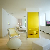White hotel room in Postmodern style - seating area with armchair, egg-shaped object and classic upholstered sofa and ottoman reflected in yellow-tinted mirror
