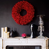 Kerzen und Vasen auf weißem Stein Kaminsims und Kranz aus roten Rosen an schwarzer Wand