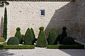 Topiary box bushes and hedges cut in various shapes on gravel surface against stone facade