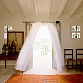 Ethnic rug in front of open terrace doors with billowing curtains and view of chair outside