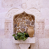 Krug und Blätterzweige auf gemauerter Ablage in orientalisch gestalteter Nische mit Bruchsteinen gefliest