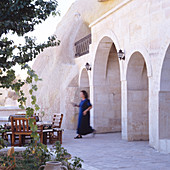 Frau geht zum Sitzplatz auf Terrasse vor orientalischem Haus mit Arkaden