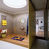 Wohnung im Loftstil mit Bullauge in der Trapezblechdecke und einer Schiebewand vor dem futuristischen Badezimmer im Stilmix mit einem Holzpodest