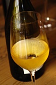 A glass of white wine in front of a bottle