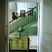 Rustic cabinet and rusty fridge in green and white stairwell; fresh flowers create a cheerful atmosphere