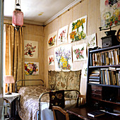 Zimmerecke mit schlichtem Bett und darüberhängenden, fröhlichen Blumenaquarellen