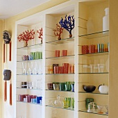 Coloured drinking glasses on fitted shelving with glass shelves