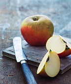 Apple wedges and a whole apple with a knife on a chopping board
