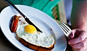 A man eating an English breakfast - fried egg and sausages