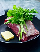 Beef, a slice of butter and a punch of parsley in a pan