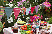 A table laid in a garden with biscuits, fresh vegetables, jam and cake