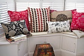 Colourful, patterned scatter cushions on window seat with integrated cupboards in bay window