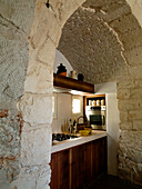 Blick durch Rundbogen aus Naturstein auf schlichte Küchenzeile in einem Trullo