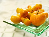 A Tangerine Surrounded by Kumquats on a Glass Plate