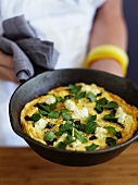A woman holding a cheese and herb omelette in a pan