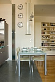 Gedeckter Esstisch in offener Küche vor schmaler Wandscheibe mit mehreren Uhren an Wand