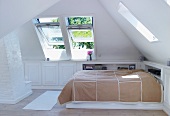 Bed with bedspread in corner of bright attic room with open dormer windows