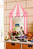 Toys on cabinet in front of mirror with whimsical frame leant on a stone wall
