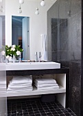 Modern washstand with towels in open-fronted shelves below next to dark marble wall