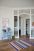 Bureau against wall and multi-coloured rug on herringbone parquet flooring in front of doorway with white-painted lattice frame