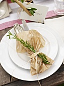 Cutlery wrapped in baking paper decorated with a sprig of rosemary and a place card
