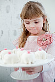 A girl in a pink dress holding a cake stand of mini cakes