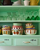 Detail of kitchen shelves holding glasses and bowls in a mixture of Art Deco and 70s styles