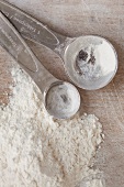 Two measuring spoons next to a pile of flour (seen from above)