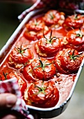 Hands holding a baking tin of stuffed tomatoes