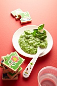 Baby food with green vegetables on a plate next to toys