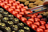 Heart-shaped pralines being picked up with a pair of tongs