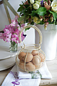 Wire basket of fresh eggs in front of bouquet of flowers