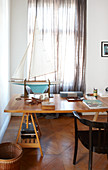 Model sailing boat on wooden table in front of window with closed, transparent curtains