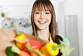 A woman holding a paper bag filled with fresh vegetables