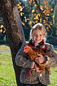 Girl against a tree trunk holding a live hen