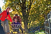 Parents pulling daughter through garden in handcart