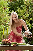 Frau schenkt Rotwein in ein Glas auf Gartentisch