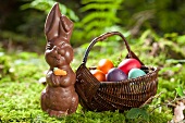 A chocolate bunny and a basket of Easter eggs in a forest