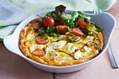 An omelette in a baking dish with goat's cheese and tomatoes