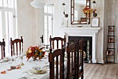 Carved wooden chairs at festively set table in simple dining room with open fireplace