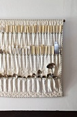 Vintage silver spoons in fabric cutlery holder hung on wall