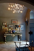 Elegant console table, framed pictures and crystal chandelier in foyer with terracotta floor tiles