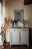 Stone vase and candelabra on wooden cabinet next to rustic standard lamp
