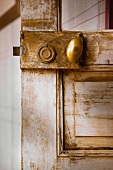 Small, oval brass doorknob on old, shabby-chic interior door